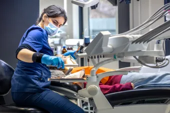 Young, female dental hygienist cleaning the teeth of a young, female patient in a sweater.