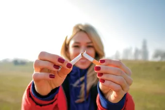 A woman holding up her hands in focus and breaking a cigarette in half.