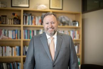 Headshot of Jay Bernhardt, Ph.D., MPH, former Dean of Moody College of Communication, current President of Emerson College, and founding director of the Center for Health Communiation at The University of Texas at Austin. A white man with a graying beard in a gray suit and orange tie.