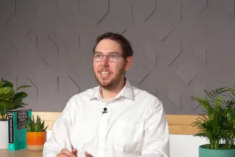 A photo of Dr. Spencer J. Fox, a white man with short, brown hair wearing glasses and a white button-down shirt sitting at a desk and talking to a camera.