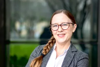 Headshot of Catherine Cunningham, a white woman with glasses and long brown hair in a braid over one shoulder wearing a white blouse and gray blazer.