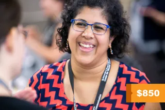 A photo of a Latina woman with short, curly dark hair wearing blue glasses, a blue and red chevron patterned blouse and smiling at another person who is out of focus. In the bottom corner is the reduced registration cost for the 2025 Health Communication Leadership Institute of $850.