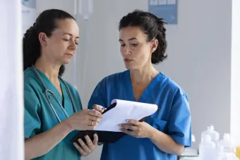 Two female doctors stand together looking over a medical chart.
