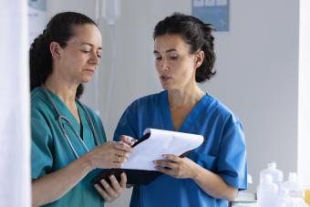 Two female doctors stand together looking over a medical chart.