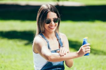College student applies sunscreen while relaxing on lawn on campus