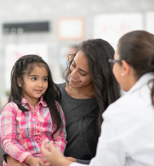 A Latina woman and her daughter sitting down and talking to a doctor