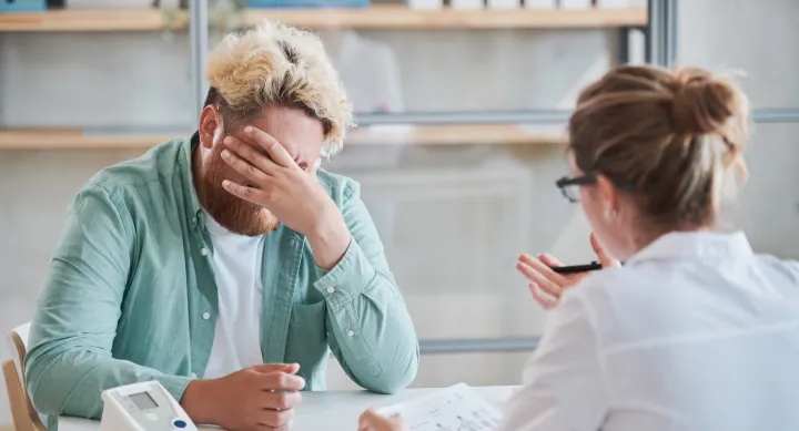 A white, female doctor speaking with a Black, male patient who is visibly frustrated