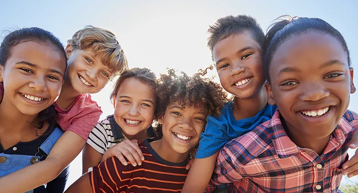 A collection of young children, male, female, Black, white, and Latinx hugging and smiling at the camera