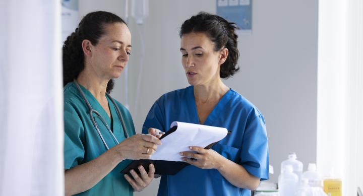 Two female doctors standing together and looking over a medical chart.